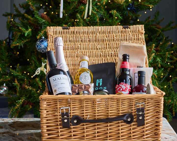 Wicker gift basket with products in front of a decorated Christmas tree